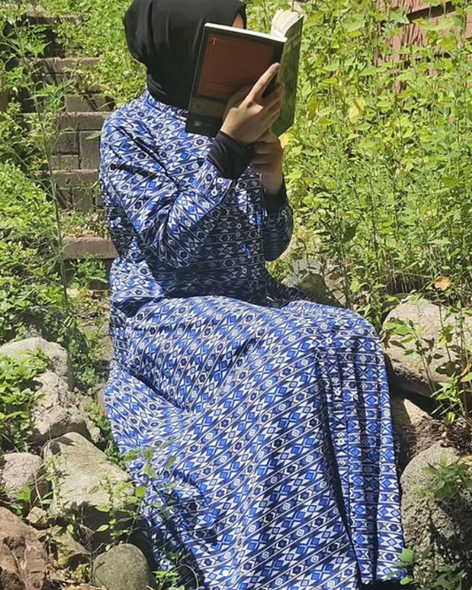 Person in a blue patterned dress sitting on stone steps reading a book outdoors.