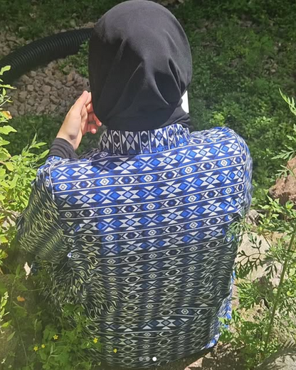 Person wearing a blue and black patterned garment sitting among green plants.